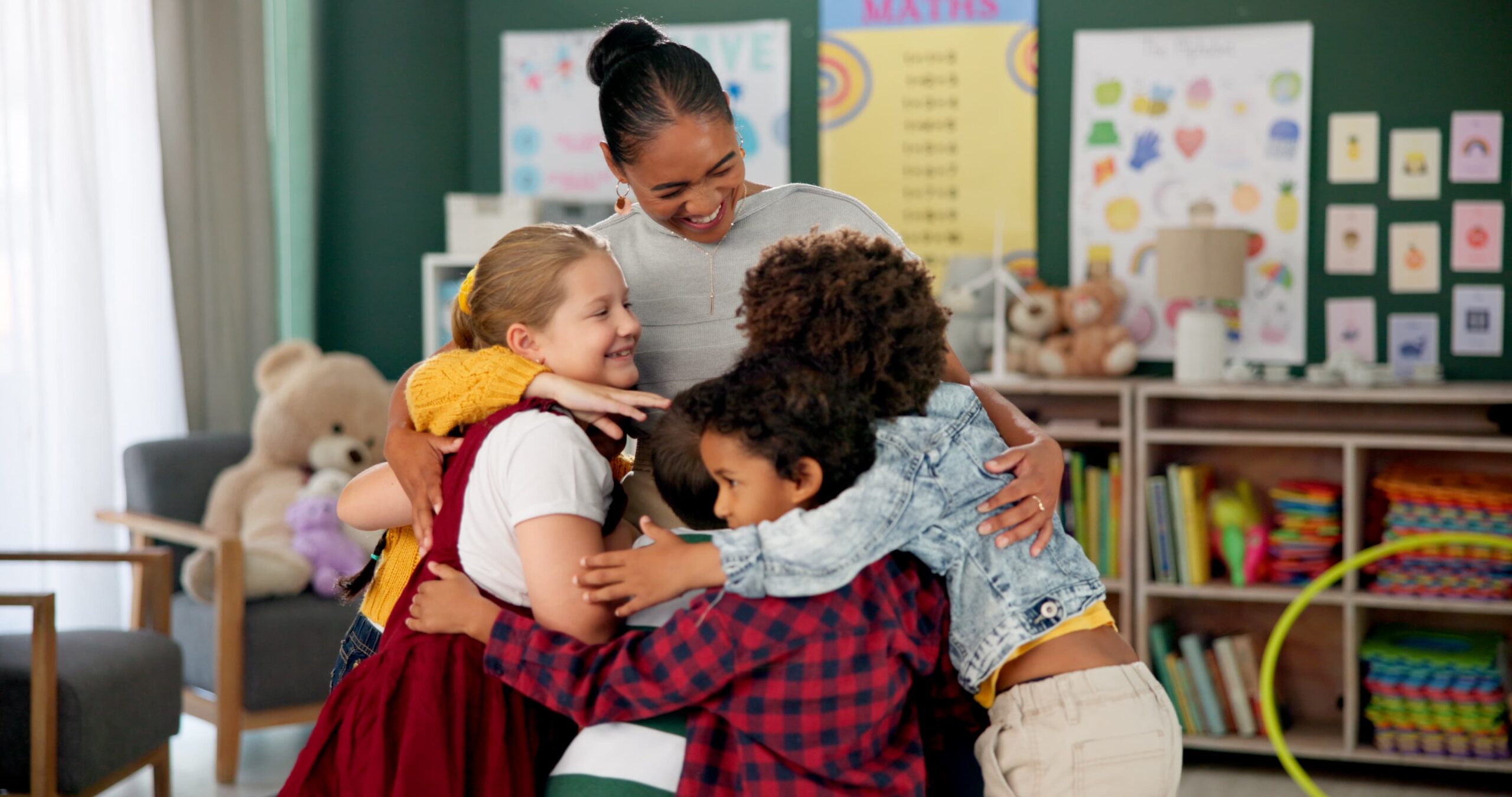 A teacher embraces several children in a warm classroom setting, fostering a sense of comfort and support.